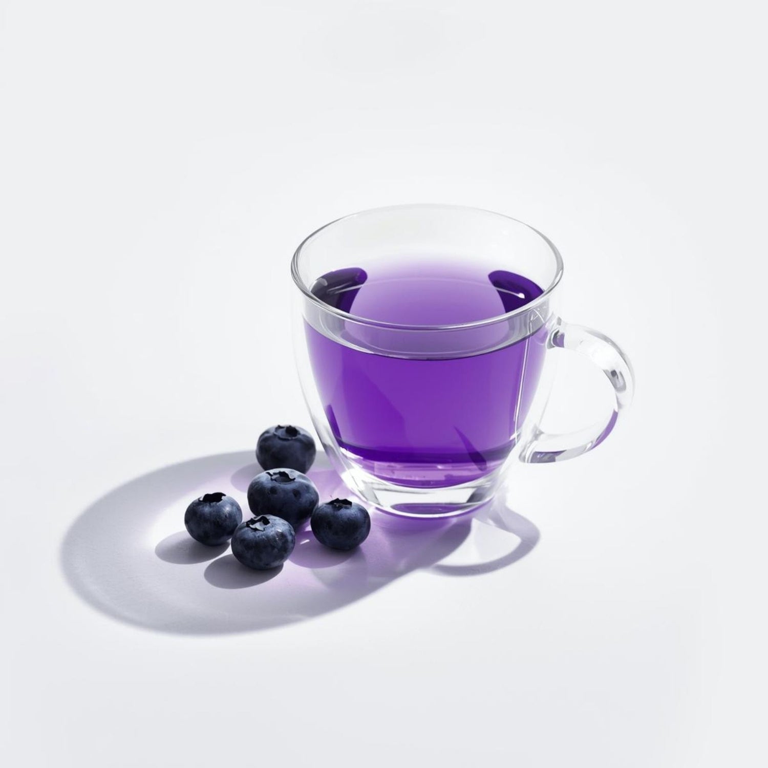 Glass cup of purple tea beside fresh blueberries on a white background